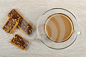 Whole cookie with caramel, cocoa and cereals, halves of cookie, cup of coffee with milk on saucer on wooden table. Top view