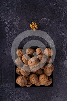 Whole and cracked walnuts on a square plate on blue textured surface, top view. Healthy nuts and seeds composition.