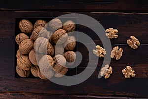 Whole and cracked walnuts on a square plate on wooden table, top view. Healthy nuts and seeds composition.