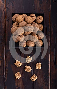 Whole and cracked walnuts on a square plate on wooden table, top view. Healthy nuts and seeds composition.