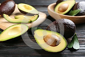 Whole and cut avocados with green leaves on dark wooden table, closeup photo