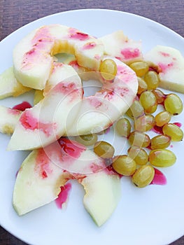whole and cut fresh peaches and a bunch of grapes on a green leaf shaped plate