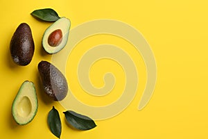 Whole and cut ripe avocadoes with green leaves on yellow background  flat lay. Space for text