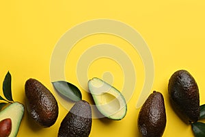 Whole and cut ripe avocadoes with green leaves on yellow background  flat lay. Space for text