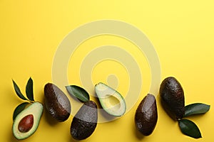 Whole and cut ripe avocadoes with green leaves on yellow background, flat lay. Space for text