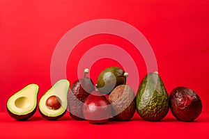 Whole and cut ripe avocadoes on red background, front view, creative. Free space for text. Avocado assortment background, banner,