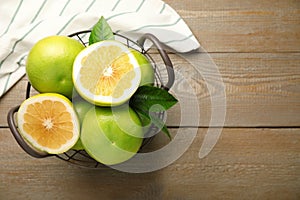 Whole and cut sweetie fruits in metal basket on wooden table, flat lay. Space for text photo