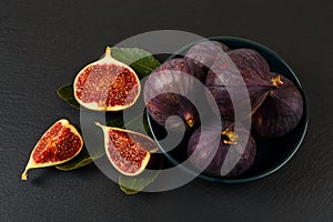 Whole and cutted fresh ripe fig fruits in a blue ceramic bowl over a black slate background. Sweet fruits and berries. Vegetarian