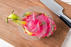 Whole dragon fruit or pitaya and sharp knife on a brown wooden cuttind board. Healthy vegetarian rich in B vitamins and tannin