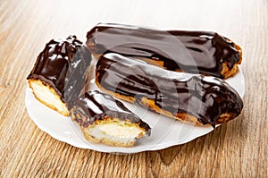 Whole eclairs and halves of eclair with chocolate in plate on wooden table