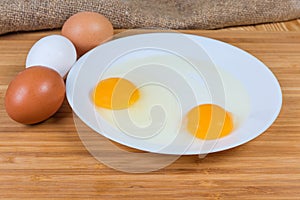 Whole eggs and broken eggs on dish on wooden surface