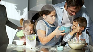 The whole family in the kitchen is preparing food. The eldest daughter stained her father with flour. Children`s joke