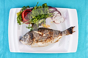 whole fish baked in the oven, served with a salad of vegetables, greens, arugula, onion rings, tomato and lemon