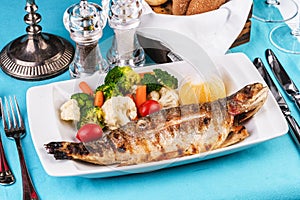 Whole fish baked in the oven, served with a salad of vegetables, greens, arugula, onion rings, tomato and lemon