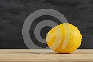 A whole fresh lemon with water droplets on a wooden table