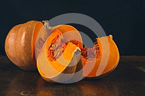 Whole fresh orange big pumpkin and slice of pumpkin on black background, closeup. Organic agricultural product