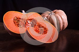 Whole fresh orange big pumpkin and slice of pumpkin on black background, closeup. Organic agricultural product