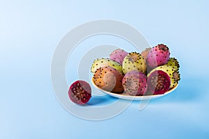 Whole fresh prickly pear fruit in a plate and cut in half an opuntia on a pastel blue background backdrop. Minimalism photo