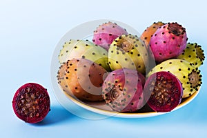 Whole fresh prickly pear fruit in a plate and cut in half an opuntia on a pastel blue background backdrop. Minimalism photo