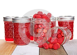 Whole fresh raspberries in open mason jars and jars of jam on table