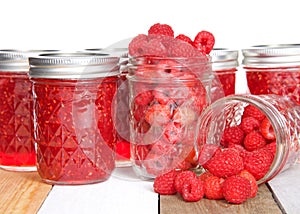 Whole fresh raspberries in open mason jars and jars of jam on table