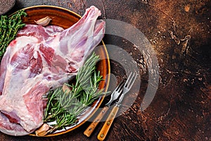 Whole fresh Raw lamb shoulder meat on a plate. Dark wooden background. Top view. Copy space