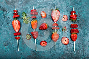 Whole fresh red strawberries and sliced strawberries on wooden skewers