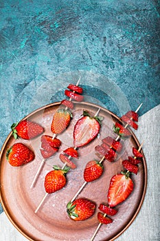 Whole fresh red strawberries and sliced strawberries on wooden skewers in ceramic plate