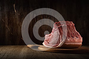 a whole freshly cut piece of raw pork loin lies on a cutting board on a brown wooden background. side view. artistic moody photo