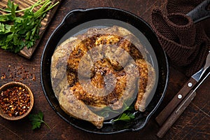 Whole fried chicken tabaka on cast iron pan, old wooden background