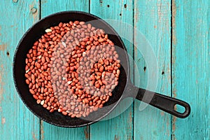 Whole fried pink peanuts in black cast iron pan on turquoise ta
