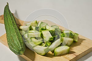 A whole gambas or luffa gourd and pieces of luffa gourd fruit on a wooden cutting board