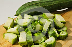 A whole gambas or luffa gourd and pieces of luffa gourd fruit on a wooden cutting board