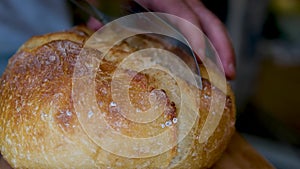 Whole grain bread put on kitchen wood plate with a chef holding gold knife for cut. Fresh bread on table close-up. Fresh