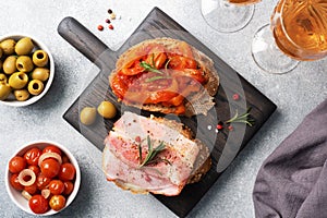 Whole grain bread sandwiches with cream cheese, bacon and canned peppers with tomato on a wooden cutting Board. Gray concrete