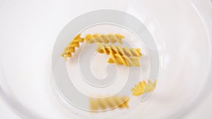 Whole grain dark yellow uncooked fusilli pasta. Italian macaroni falling in a pile in a transparent empty plate close up