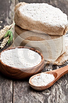 Whole grain flour in a wooden bowl and sackcloth bagwith ears