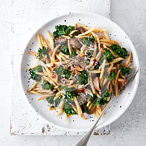 Whole grain pasta with kale, mushrooms, parmezan cheese in white plate on light background photo