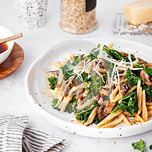 Whole grain pasta with kale, mushrooms, parmezan cheese in white plate on light background photo