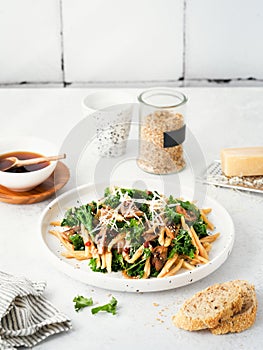 Whole grain pasta with kale, mushrooms, parmezan cheese in white plate on light background photo