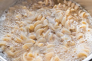 Whole grain pasta in a pan with boiling water and a spoon. Cooking healthy food