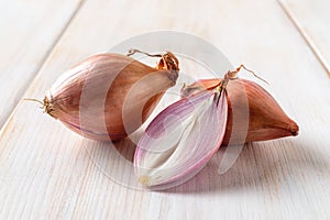 Whole and half red eschalots on a white wooden table. Close-up of unpeeled long shallot bulbs. Fresh raw onion ready for cooking.