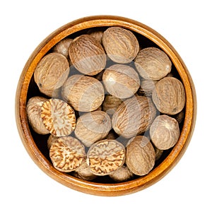 Whole and halved nutmegs, dried seeds, in a wooden bowl