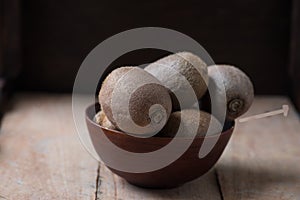 Whole kiwi fruit in a bowl on rustic wooden background