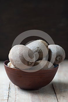 Whole kiwi fruit in a bowl on rustic wooden background