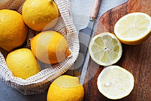 Whole lemons next to cut ones on a wooden board next to a knife