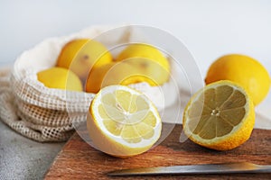 Whole lemons next to cut ones on a wooden board next to a knife