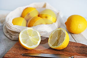 Whole lemons next to cut ones on a wooden board next to a knife