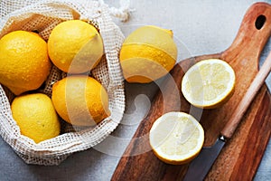 Whole lemons next to cut ones on a wooden board next to a knife