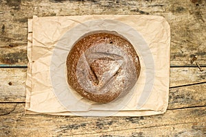 Whole loaf of bread with paper bag on weathered wood background